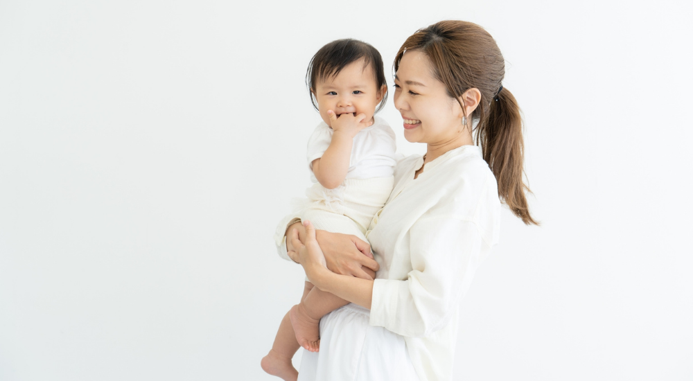 白背景で笑顔の母親が赤ちゃんを抱っこしている画像で、【体幹・上肢帯(骨盤底筋群・腹横筋・上腕二頭筋周辺)】を示し、産後の骨盤ケアやインナーマッスルの回復によって、負担のかかりやすい抱っこ姿勢でも腰や手首の痛みを起こさずに楽しく育児と向き合えている様子。