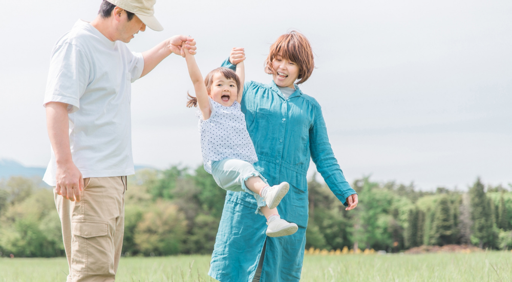 緑豊かな公園で両親が幼い娘の両手を引いて元気に持ち上げて遊んでいる画像で、【腰部・肩関節(脊柱・ローテーターカフ周辺)】を示し、ぎっくり腰や肩の痛みの不安なく、安心して子供との触れ合いや育児を楽しめている健やかな日常の様子。